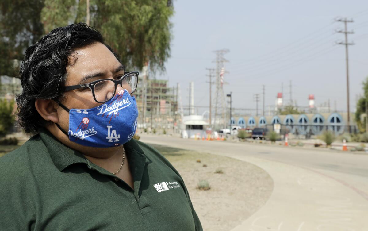 A man in a blue Dodgers face mask stands down the street from a power plant