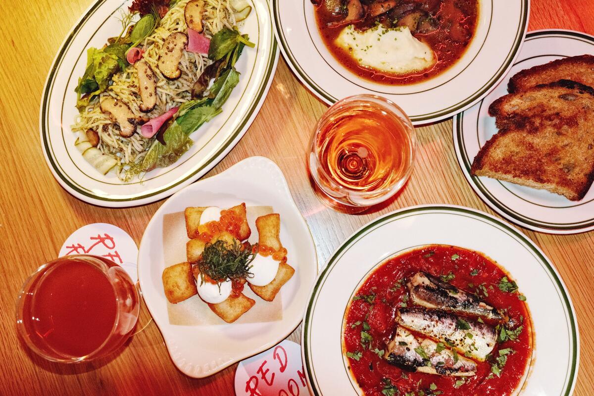 An overhead photo of a spread of Korean small plates with two glasses of wine from Red Room in Koreatown.