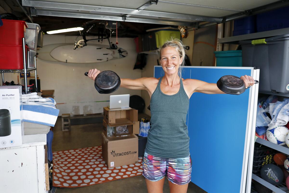 Costa Mesa resident Kelly Evans, 37, uses a pair of 5-pound iron skillets as dumbbells in her exercise routine. Due to the coronavirus pandemic, Evans was furloughed from her job as a personal trainer and fitness instructor at the Newport-Mesa YMCA. In response, she decided to continue leading her students through online classes via Zoom and by posting exercise videos on her website via YouTube.