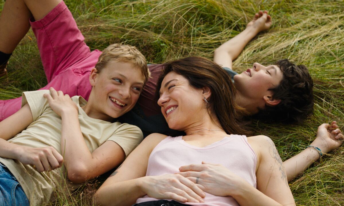 Two young teen boys lie on the grass with one's mother in a scene from "Close."