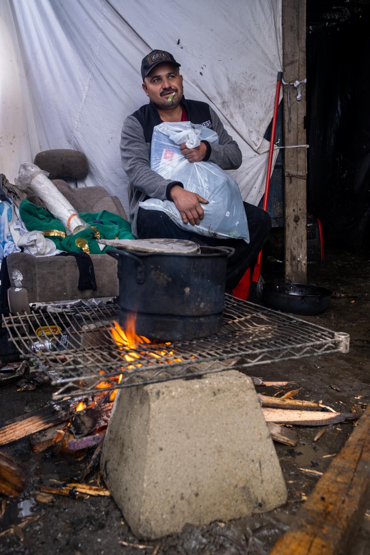 Reynaldo Roman, 39, sits in his makeshift home near a pot of beans he is cooking.