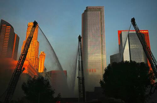 High atop ladders against the downtown L.A. skyline, firefighters direct water toward burning buildings at Broadway and Fourth Street. The blaze caused no injuries, but forced the closure of streets, snarling the Monday morning traffic.