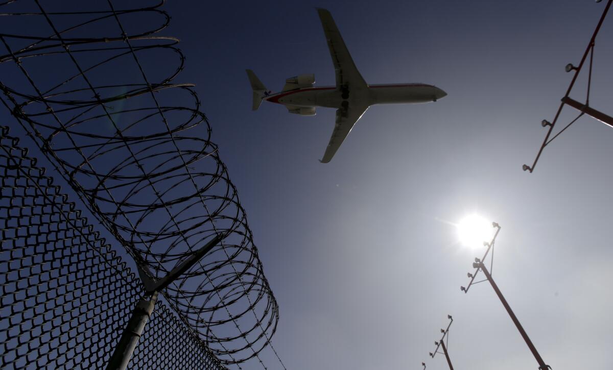 A passenger jet flies over the perimeter fence at the Los Angeles International Airport as it lands.