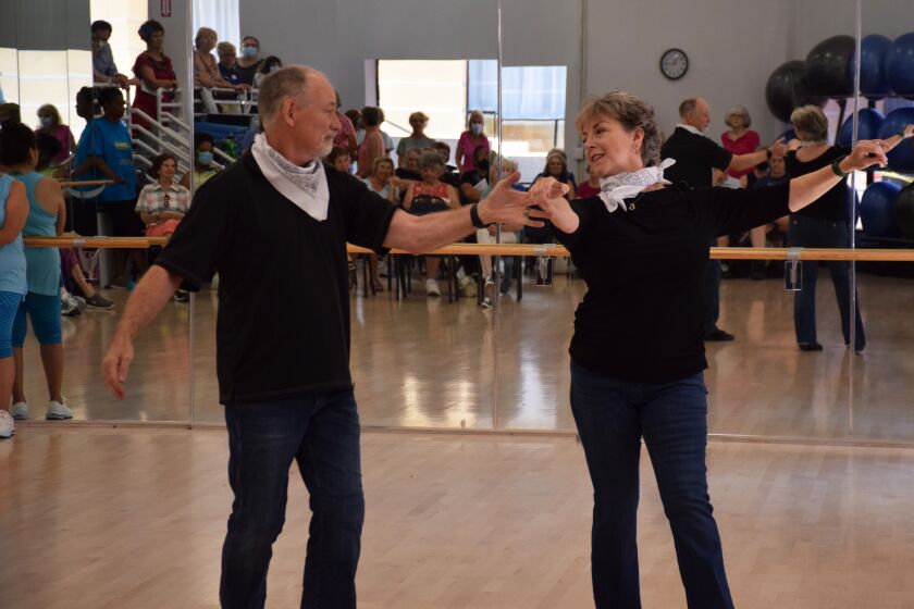a couple wearing jeans, black shirts and white bandanas demonstrate west coast swing dance