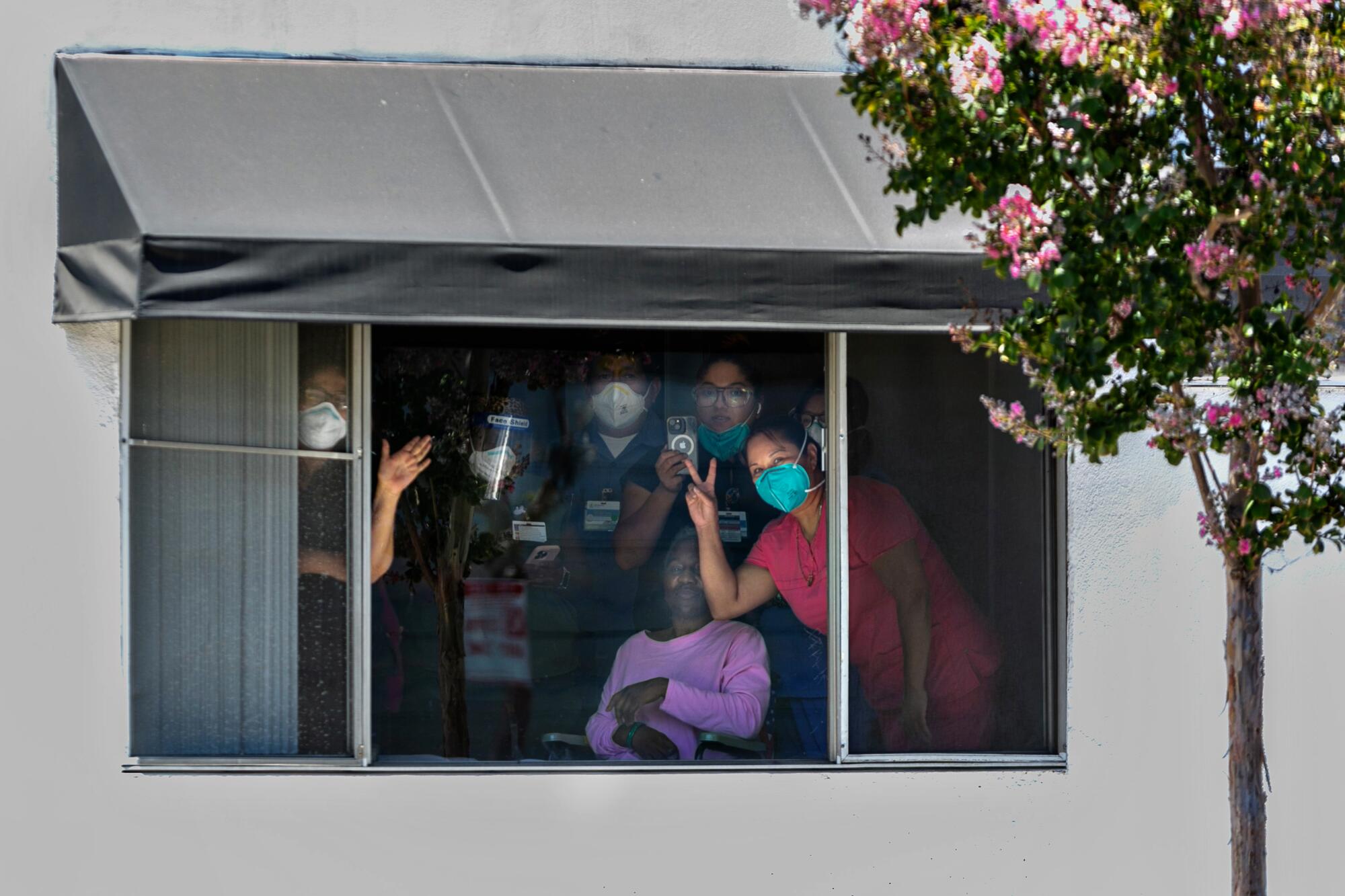 Residents and staff of a nursing facility huddle around a window to catch a glimpse of Vice President Kamala Harris 