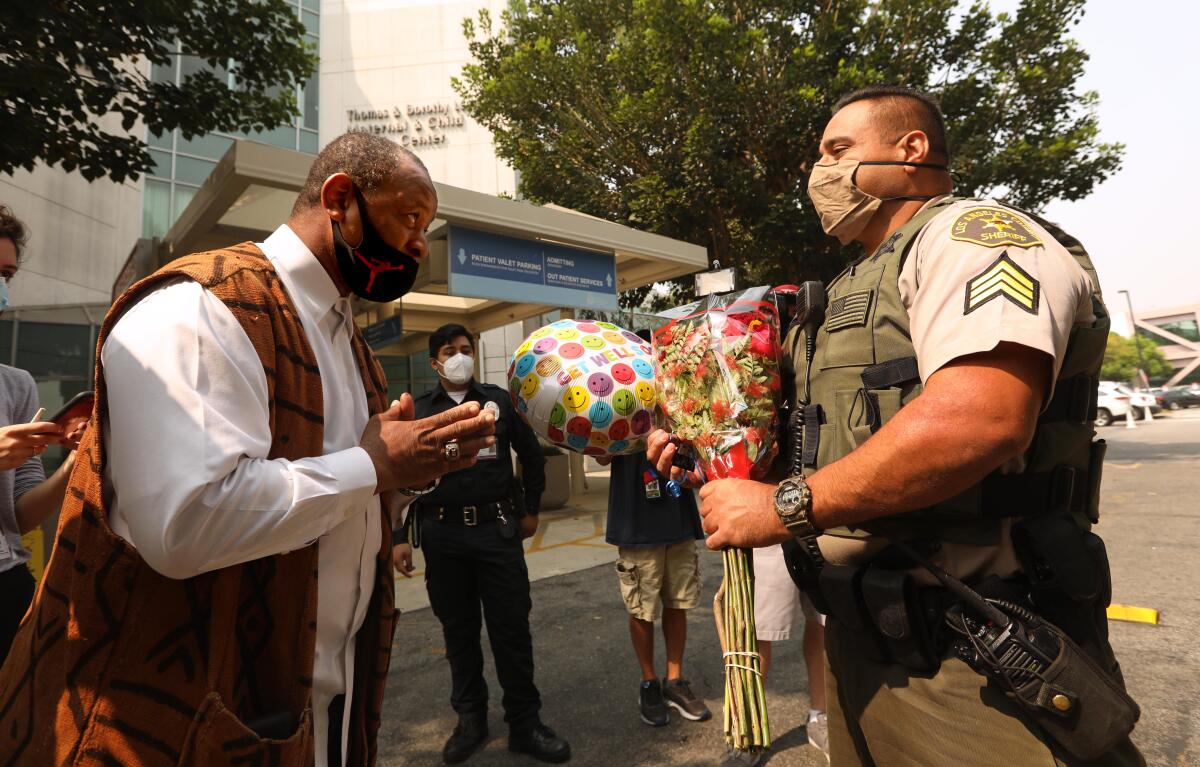 Community activist Najee Ali gives L.A. County sheriff's Larry Villareal flowers and a "get well" balloon.