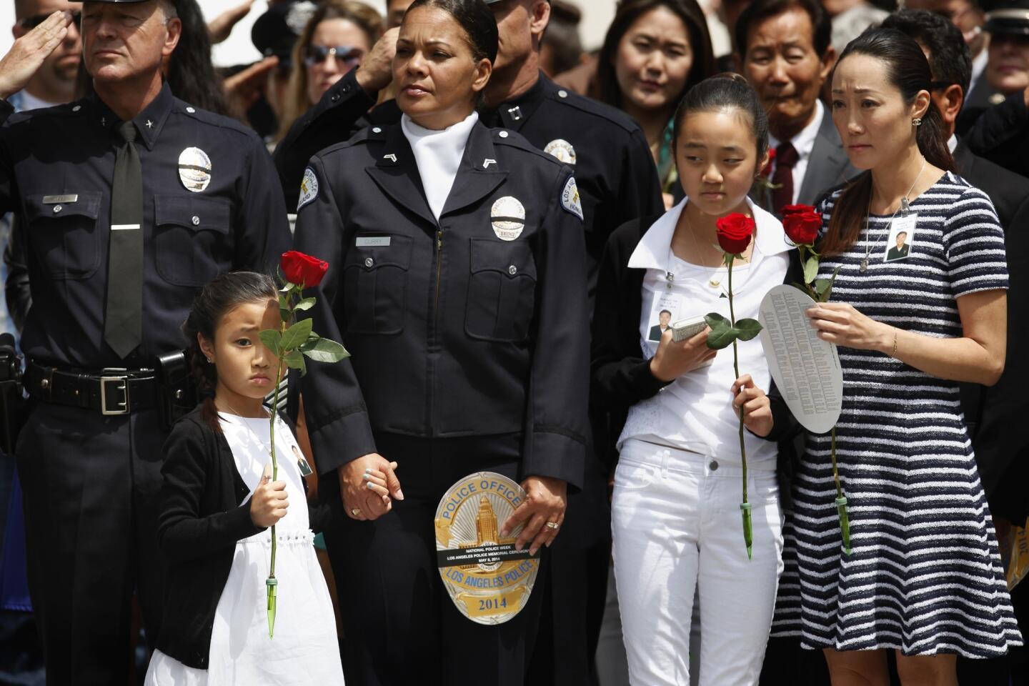 Kendall Lee, 6, left, holds a rose in one hand and the hand of LAPD officer Rosalind Curry with the other. Kendall's father, LAPD Officer Nicholas Lee, was killed this year. At right are Jalen Lee, 11, his other daughter, and Cathy Lee, his widow.