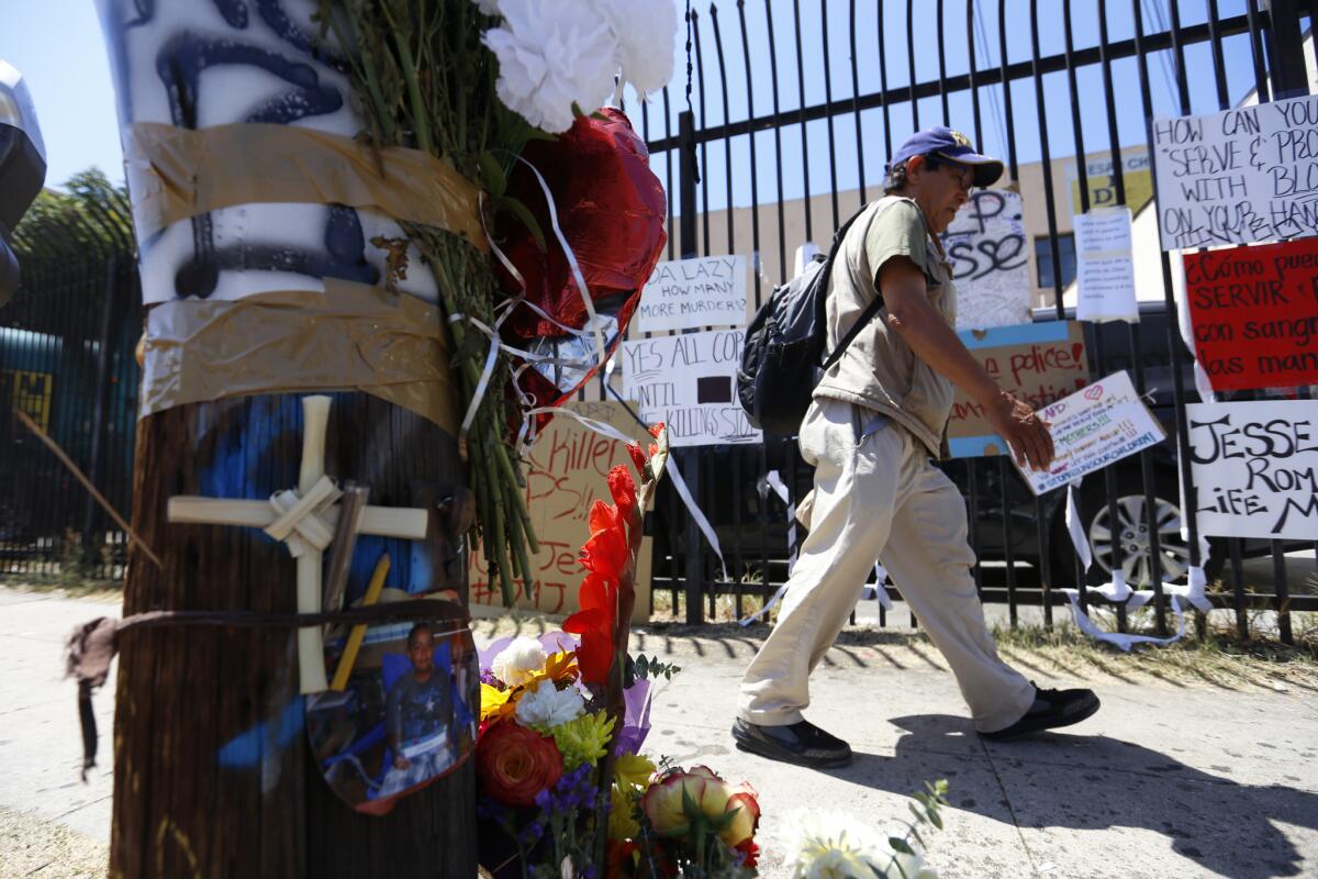 A man walks past signs, flowers, a photo and candles left near the area in Boyle Heights where Jesse Romero, 14, was shot by Los Angeles police last week.