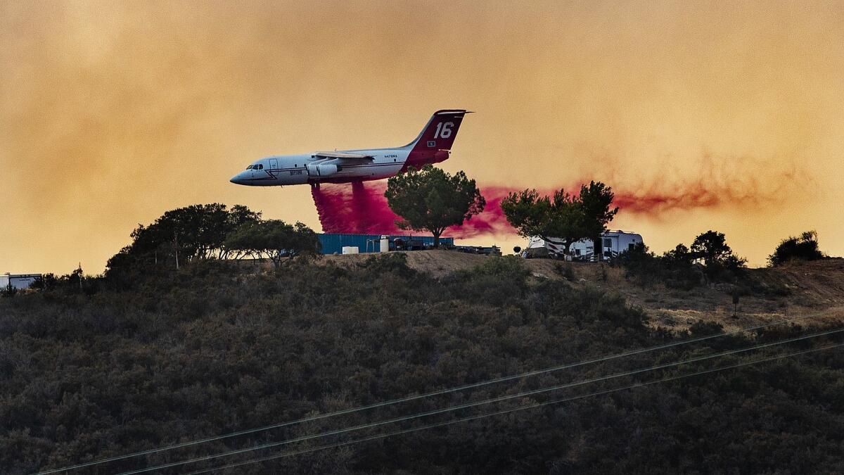 An air tanker flies low to drop fire retardant near campers and trailers on a mountain ridge to fight the Holy fire on Aug. 11, 2018.