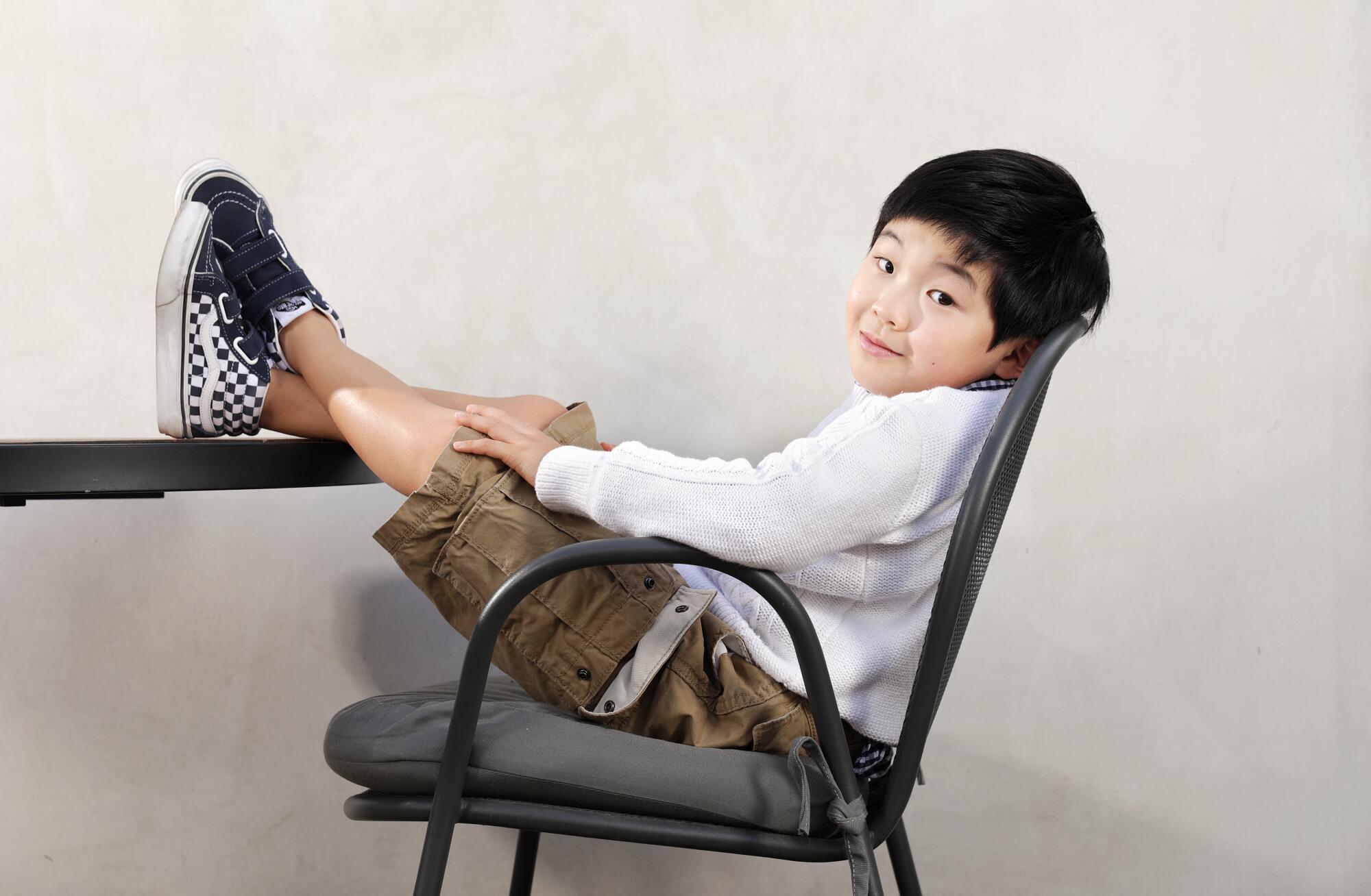 Eight-year-old Alan Kim sits with his feet up on a desk.