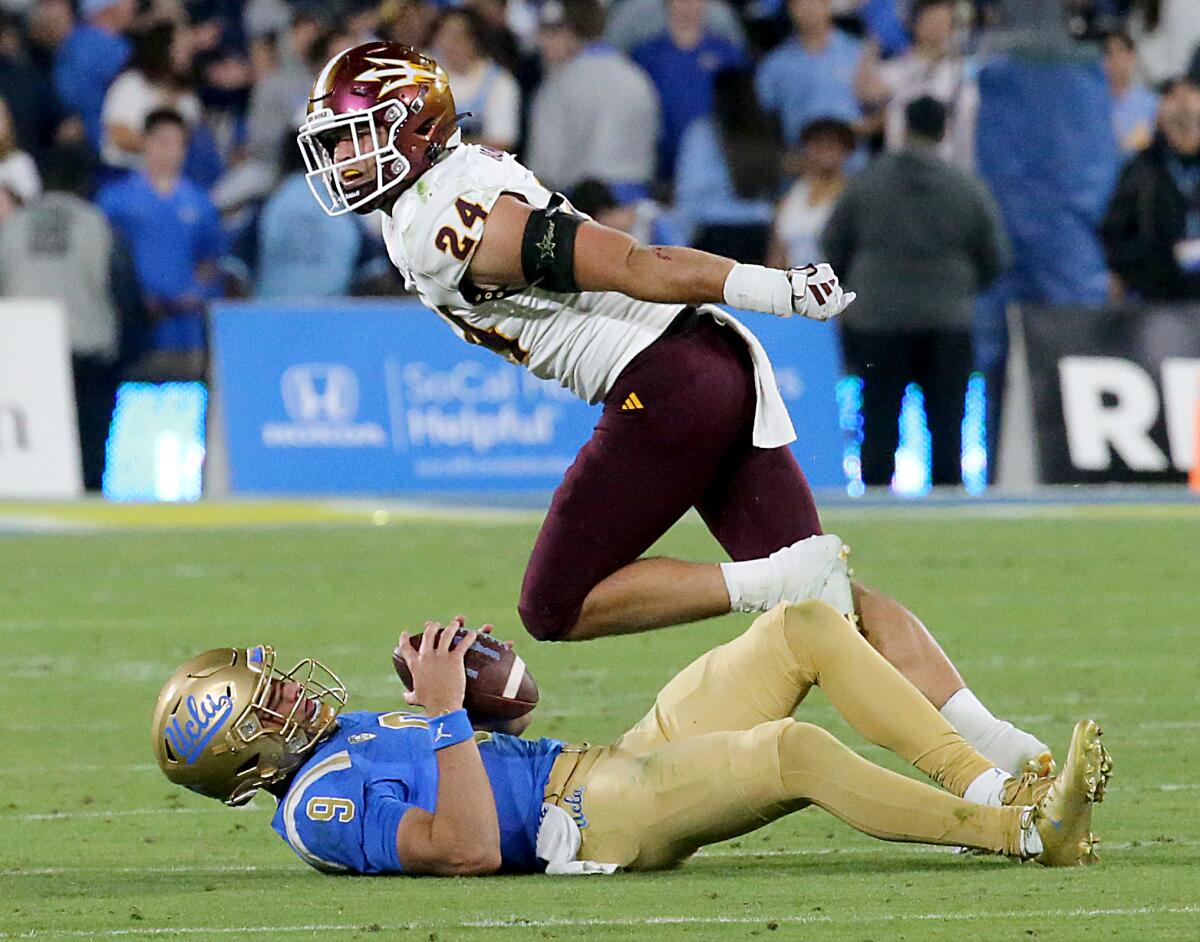 Arizona State linebacker Tate Romney holds out his arm while Colin Schlee is nearby on the ground holding the ball.