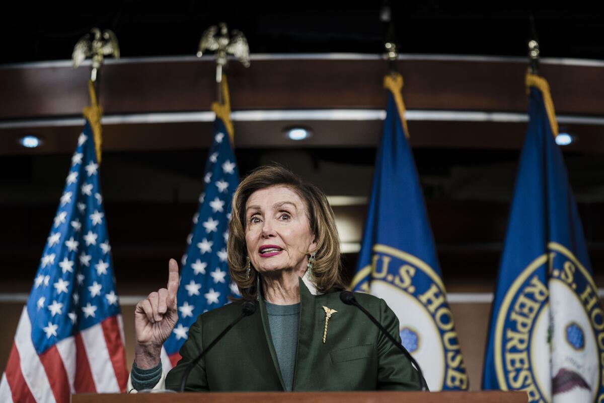 House Speaker Nancy Pelosi stands at a lectern in front of flags.