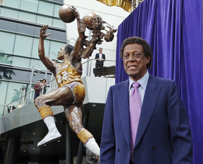 Elgin Baylor, right, in a blue suit and a tie, stands next to a statue of a basketball player in Laker uniform