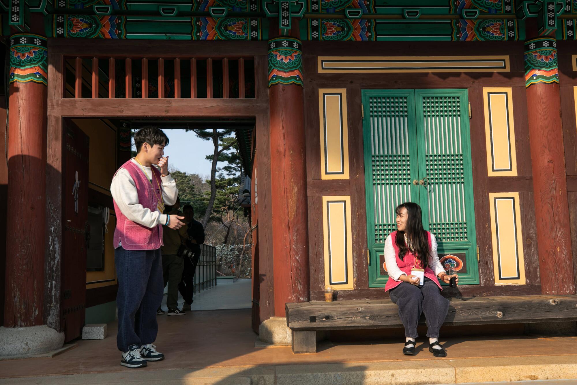 A man standing on the left speaks to a woman seated on a temple bench 