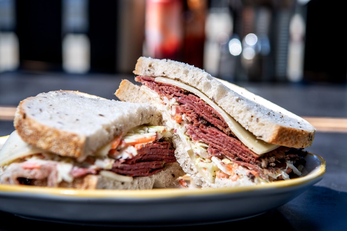 A pastrami sandwich, cut in half, on a plate.