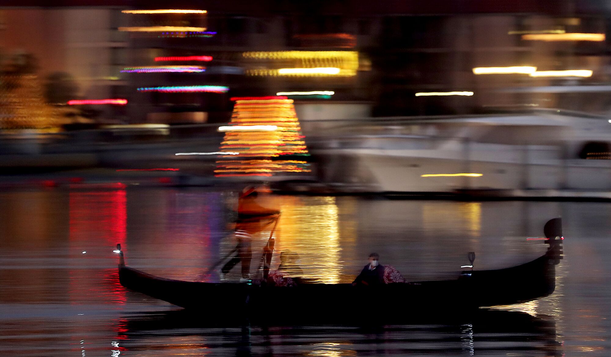 Holiday lights reflect off Alamitos Bay as a gondolier takes a single passenger for a ride on Dec. 8.