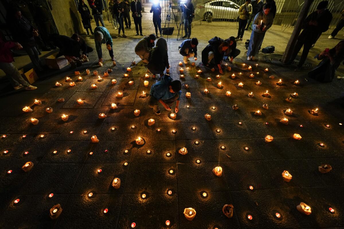 People light candles during a vigil for three police officer in front of Chile's police headquarters in Santiago, Chile, Saturday, April 27, 2024. Armed assailants ambushed and killed three law enforcement officers in southern Chile on Saturday before setting their car on fire, authorities said. (AP Photo/Esteban Felix)