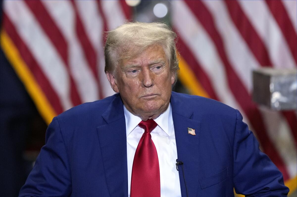 Former President Trump sits in front of American flags. 