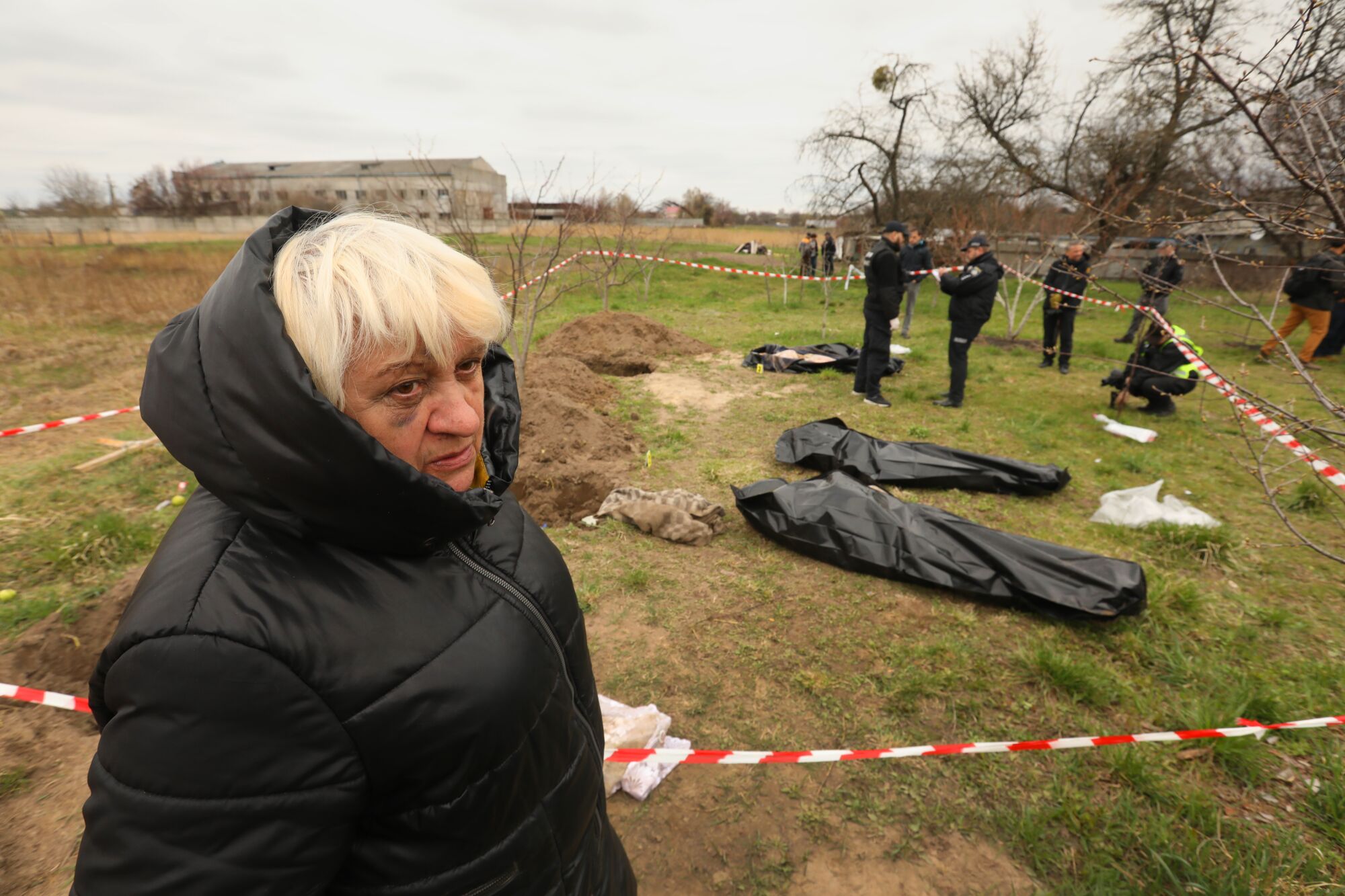 A woman stands in a field in front of bodies found in a mass grave in the town of Borodyanka