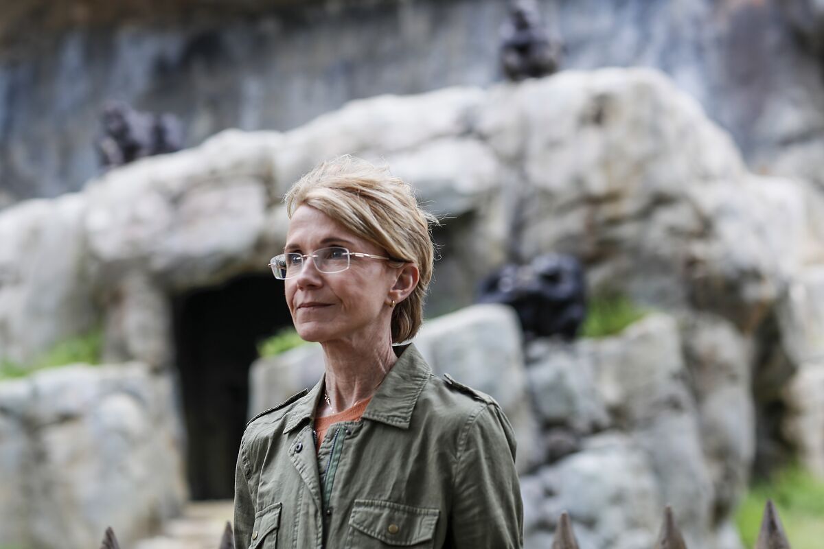 Closeup of a woman with short blond hair and glasses standing in front of a zoo enclosure.