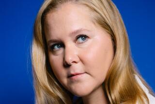 Amy Schumer looks up and to the left while posing for a portrait in a white blazer against a blue background