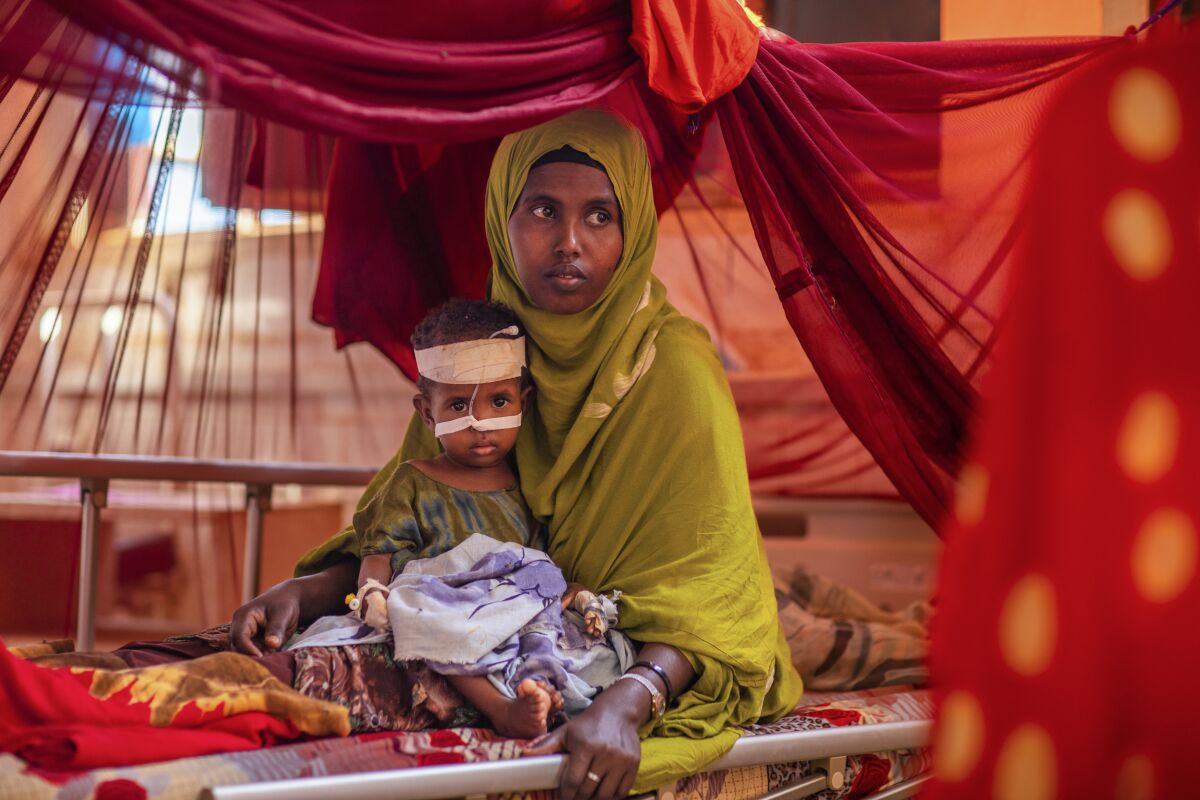 A woman and a child sit in a hospital bed under a gauzy red tent 