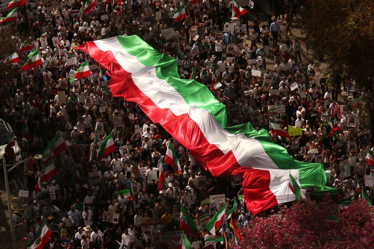 A large crowd carries a red, white and green banner