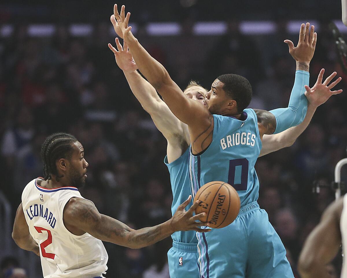 Clippers star Kawhi Leonard passes behind Charlotte Hornets defenders Cody Zeller and Miles Bridges.