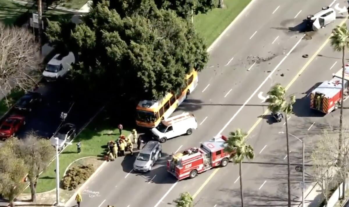 A bus, van, minivan and firetrucks at the scene of a crash where another vehicle rests on its side.