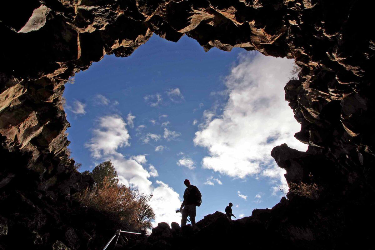From inside a cave looking out, people are seen silhouetted by blue sky.
