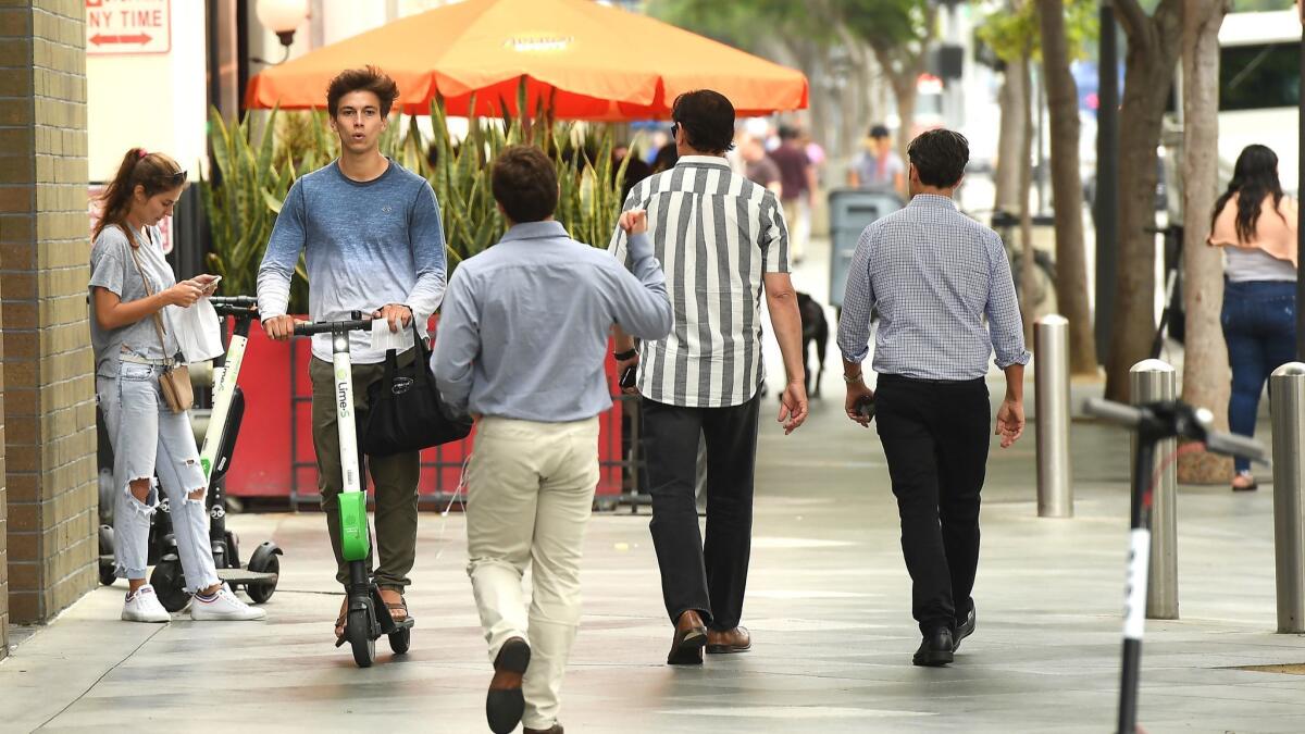 A Lime rider illegally rides a scooter on a sidewalk in Santa Monica before receiving a ticket in July 2018. Students at San Jose State no longer will be allowed to ride the electric vehicles on campus after a ban was enacted on Monday.