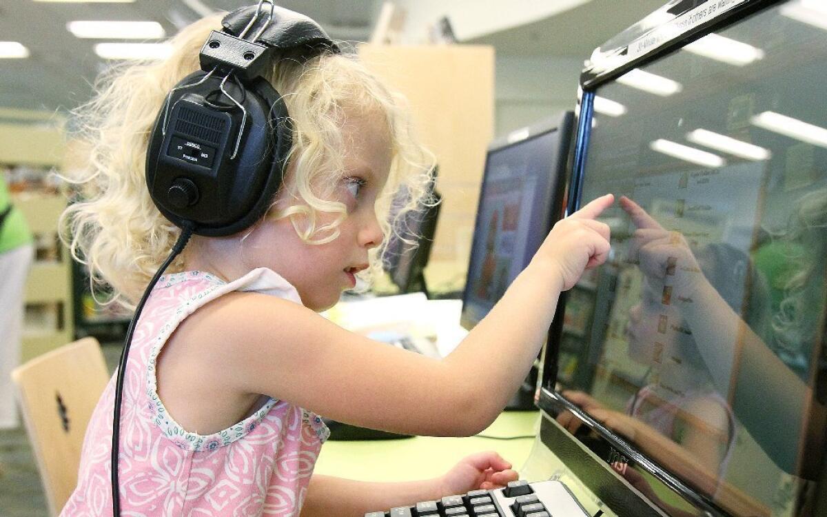 Kenley Miller, 4, of Burbank, points to what she heard in the earphones on a children's computer at the Northeast branch library on the day of reopening Monday after an extensive remodel.