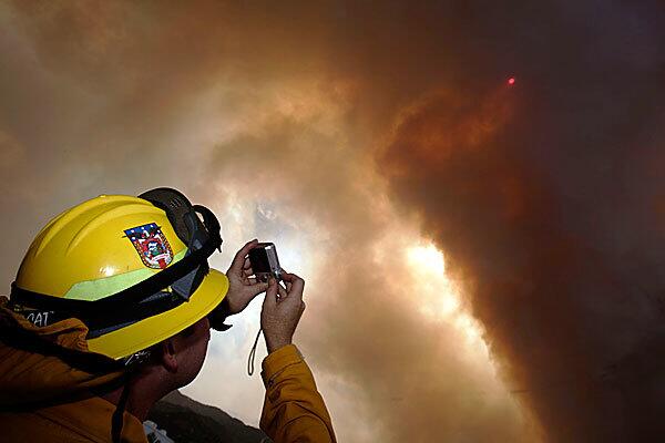 Patrick Schmitz, a firefighter from the Guadalupe Fire squad in Central California, photographs a glowing orange sun hidden behind dark smoke rising from the Station fire that creeped over the mountain in Acton overnight.