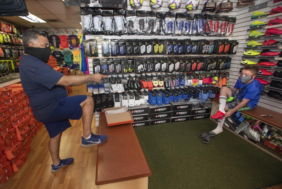 Carlos Marroquin, 53, owner of Planet Soccer, practices social distancing while talking to customer Benton Watkins, 13, of Santa Clarita, as he tries on a new pair of cleats inside the store in Newhall.