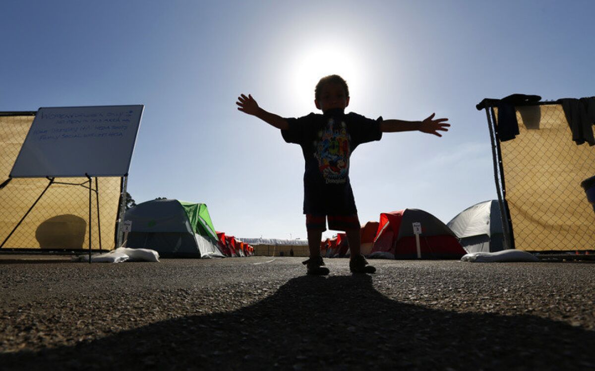 In this file photo, a child stands at the entrance to a city-sanctioned homeless camp near Balboa Park. Below, a writer says people experiencing homelessness need somewhere to go, now more than ever.