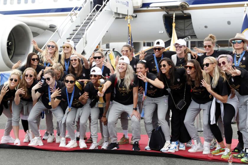 Members of the United States women's soccer team, winners of a fourth Women's World Cup, celebrate and pose with the trophy by their plane after arriving at Newark Liberty International Airport, Monday, July 8, 2019, in Newark, N.J. Julie Ertz holds the trophy, Megan Rapinoe, front right, gestures, and Alex Morgan, back left, also gestures. (AP Photo/Kathy Willens)