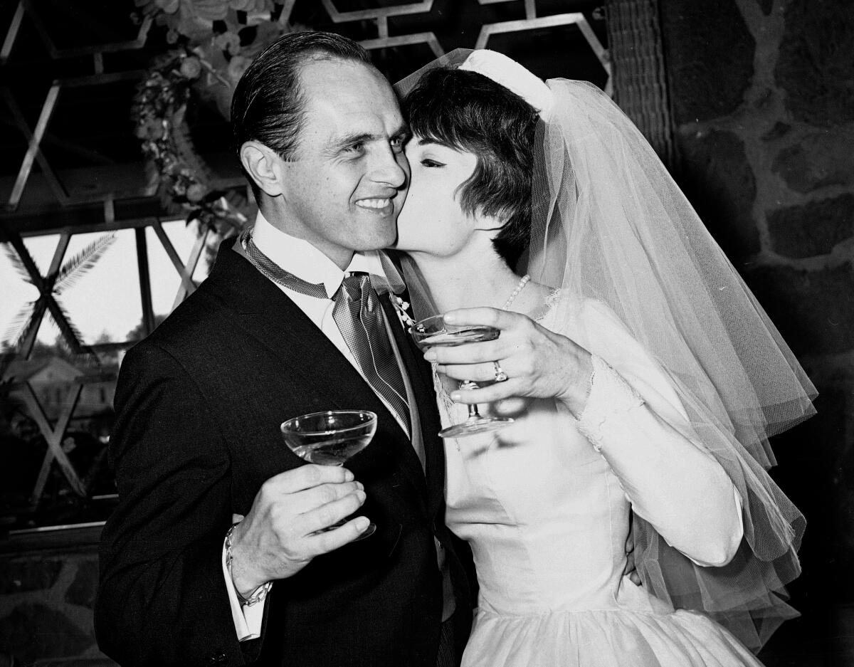 A black-and-white photo of a young Bob Newhart and wife Ginnie as they raise glasses in wedding formalwear in 1963