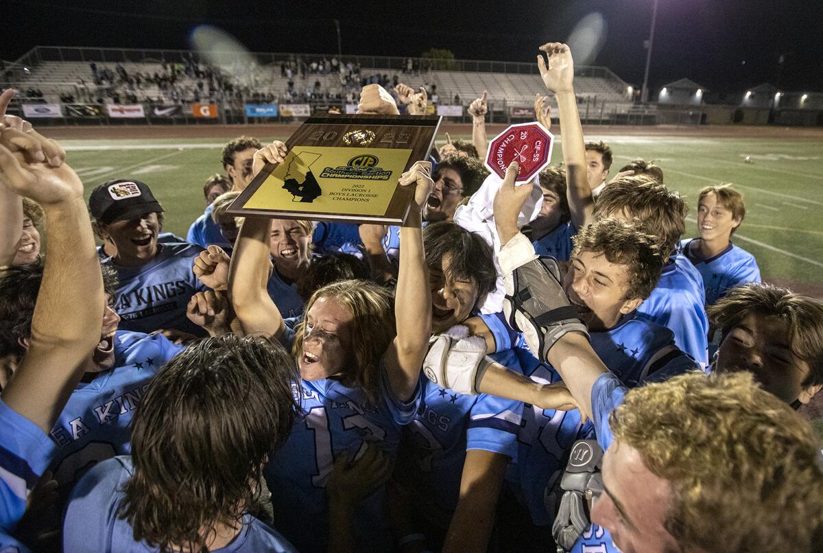 Corona del Mar's Gavin Gossen is mobbed by his teammates while holding up the championship plaque.