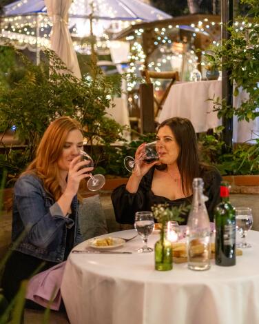 Two women drink from wineglasses at their table on the creekside patio at the Inn of the Seventh Ray.