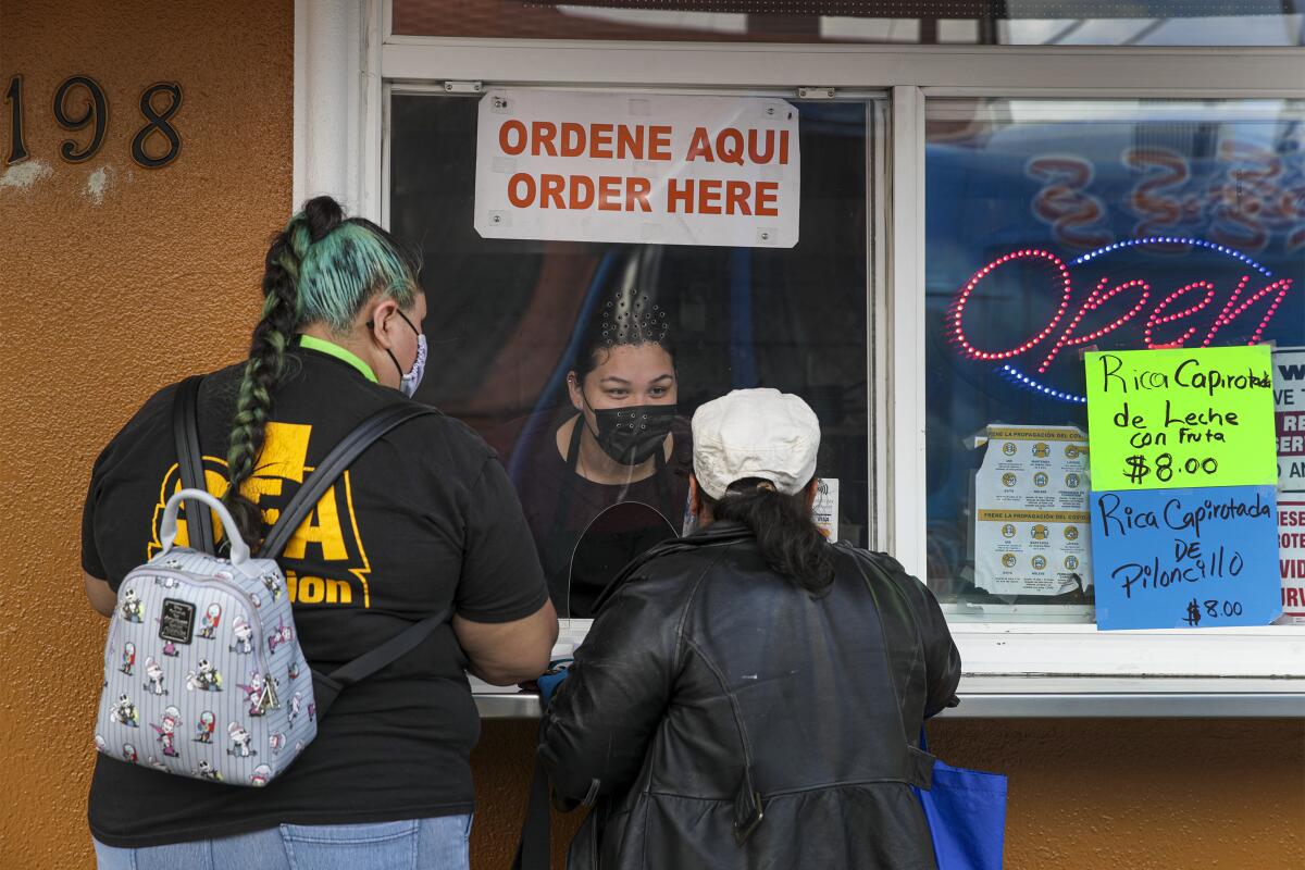 Two women speak to a restaurant worker through an order window.