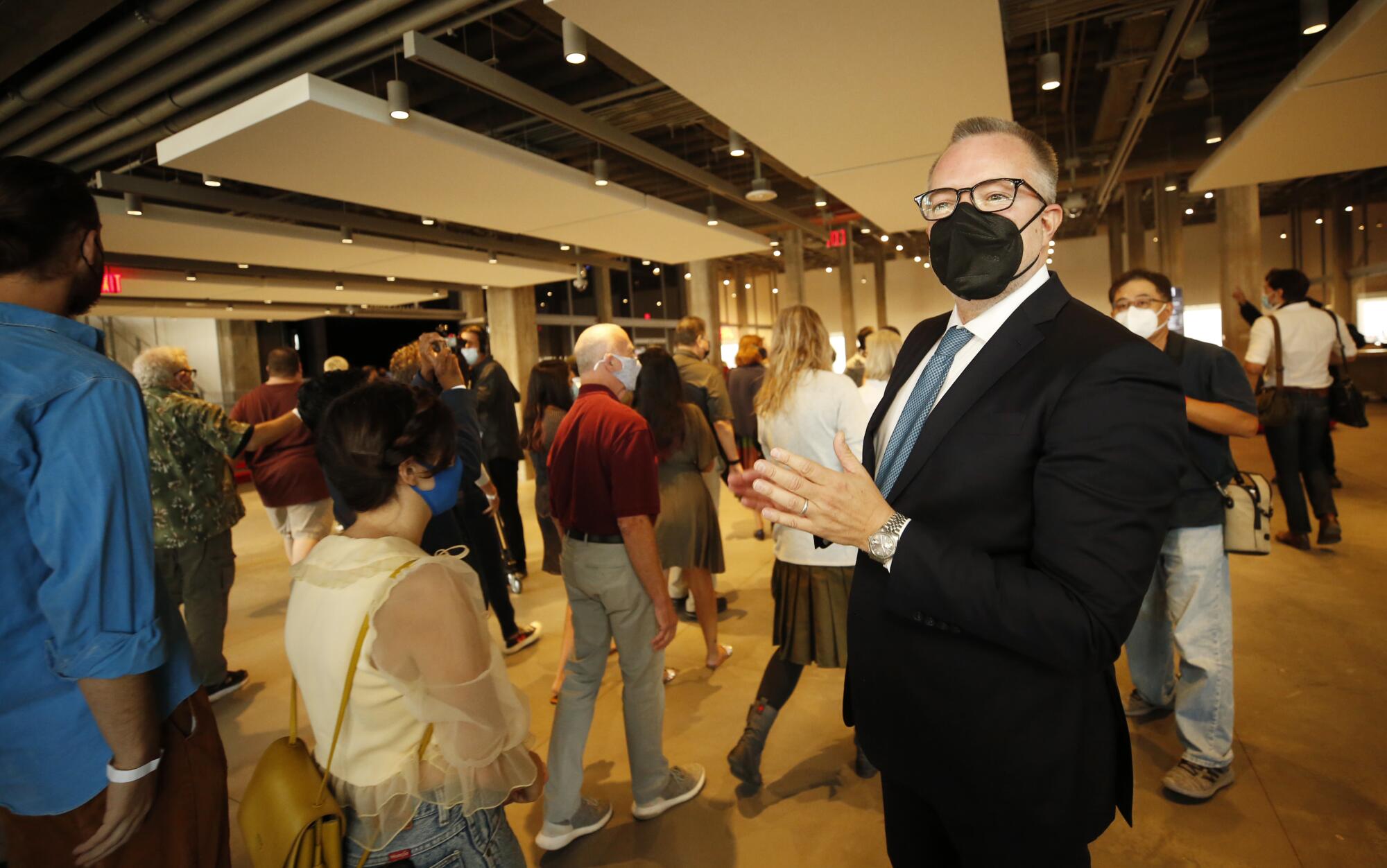 A masked man in a suit greets visitors in line to enter the Academy Museum.