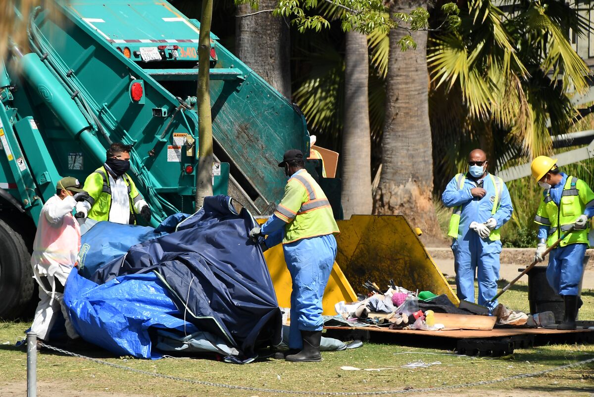 Workers in high-visibility vests load a garbage truck in a park