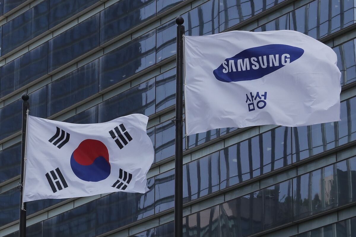 A Samsung Group flag and South Korean national flag flutter on adjacent poles outside office building