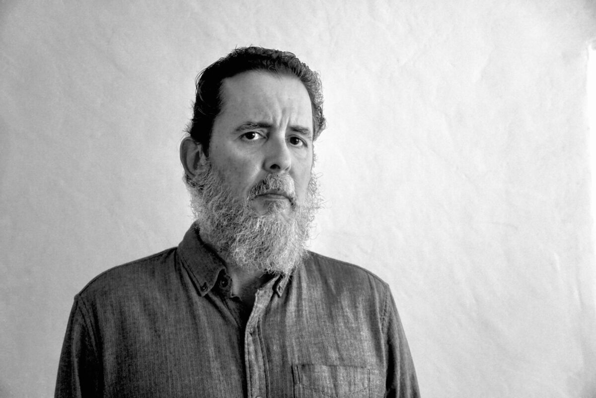 A black-and-white portrait of a bearded man in a button-down shirt 
