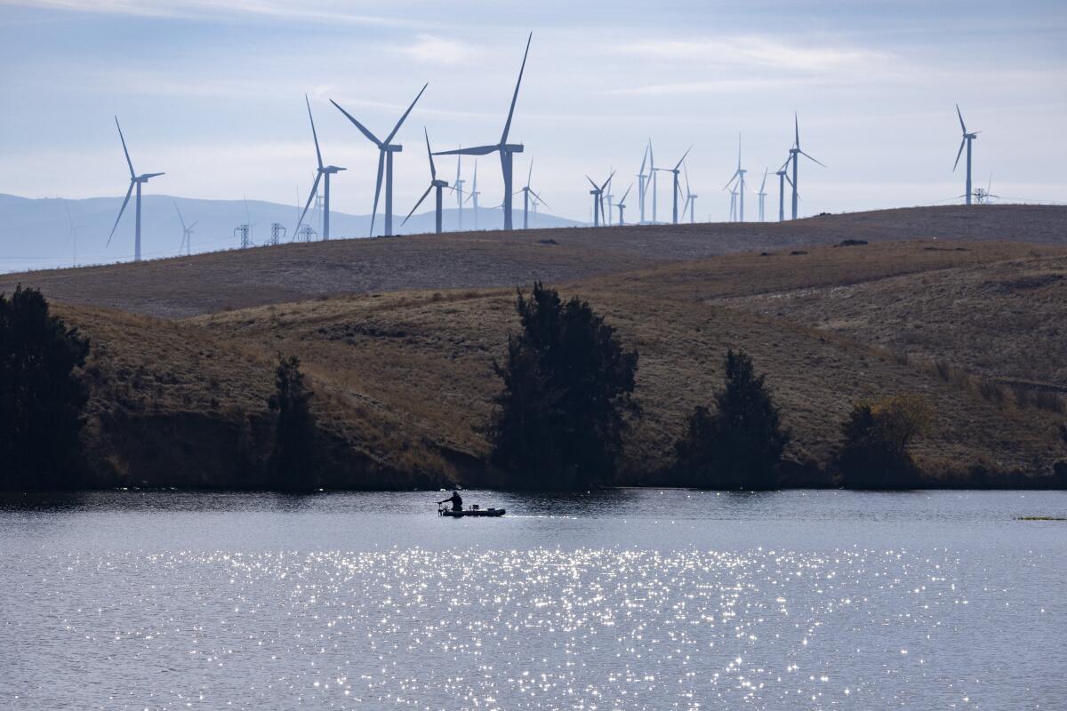 Wind turbines dot a hilly landscape near a body of water