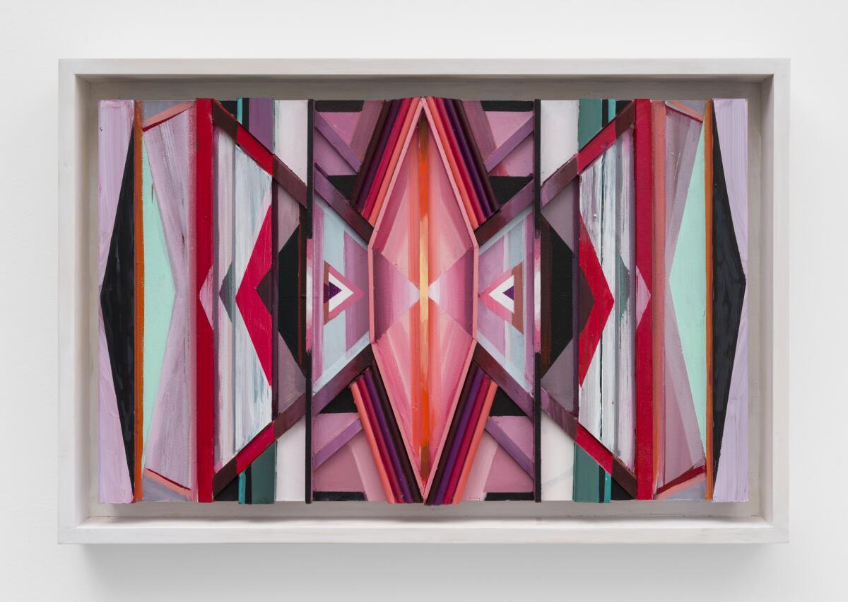 A geometric bas relief painting in shades of pink, red and aqua evokes female forms.