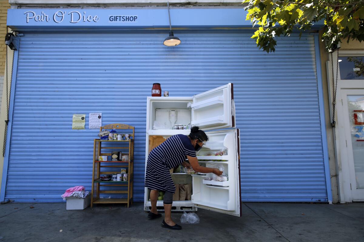 A woman restocking an open refrigerator on a sidewalk