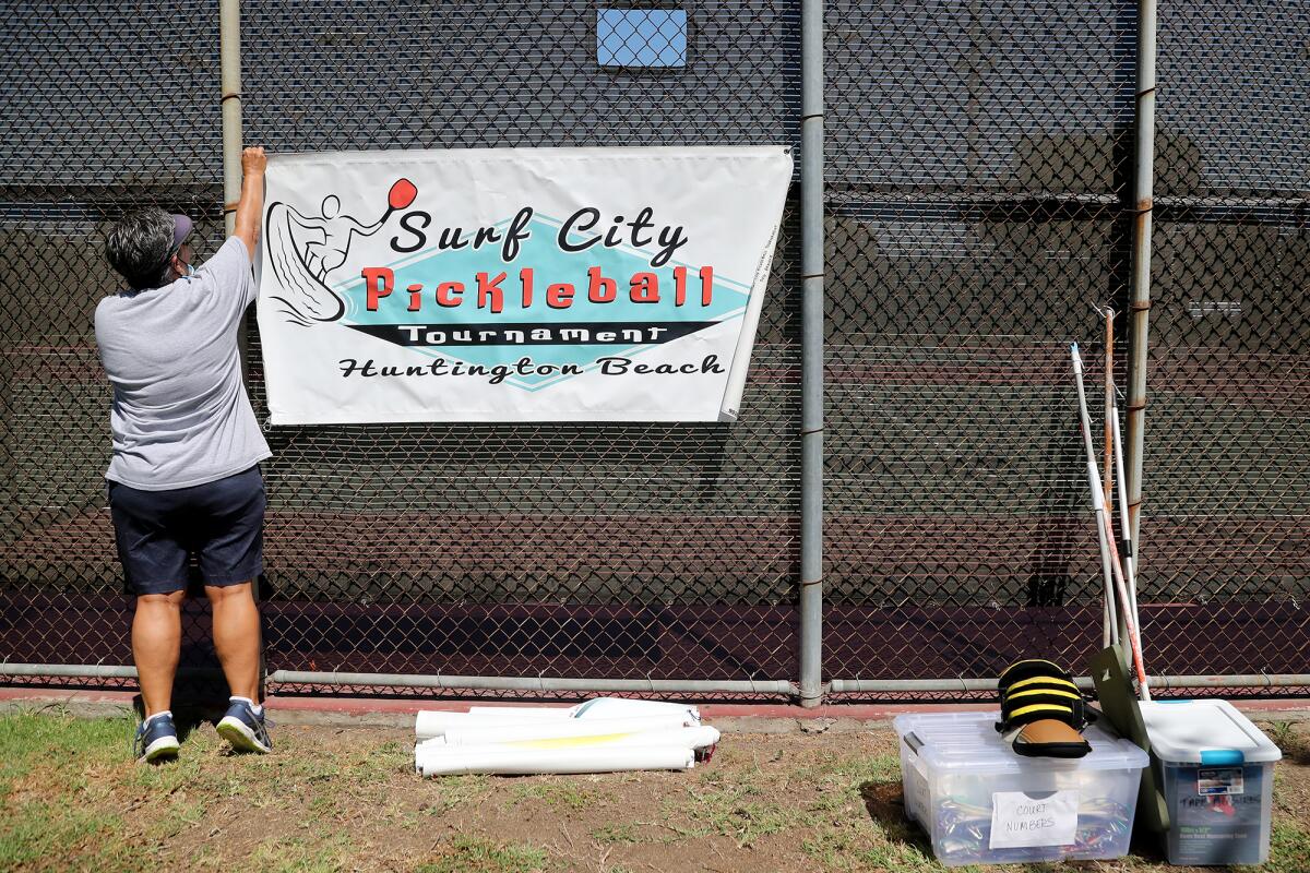 Tournament director Diana Abruscato hangs a banner for the annual Surf City Pickleball Tournament in Huntington Beach.