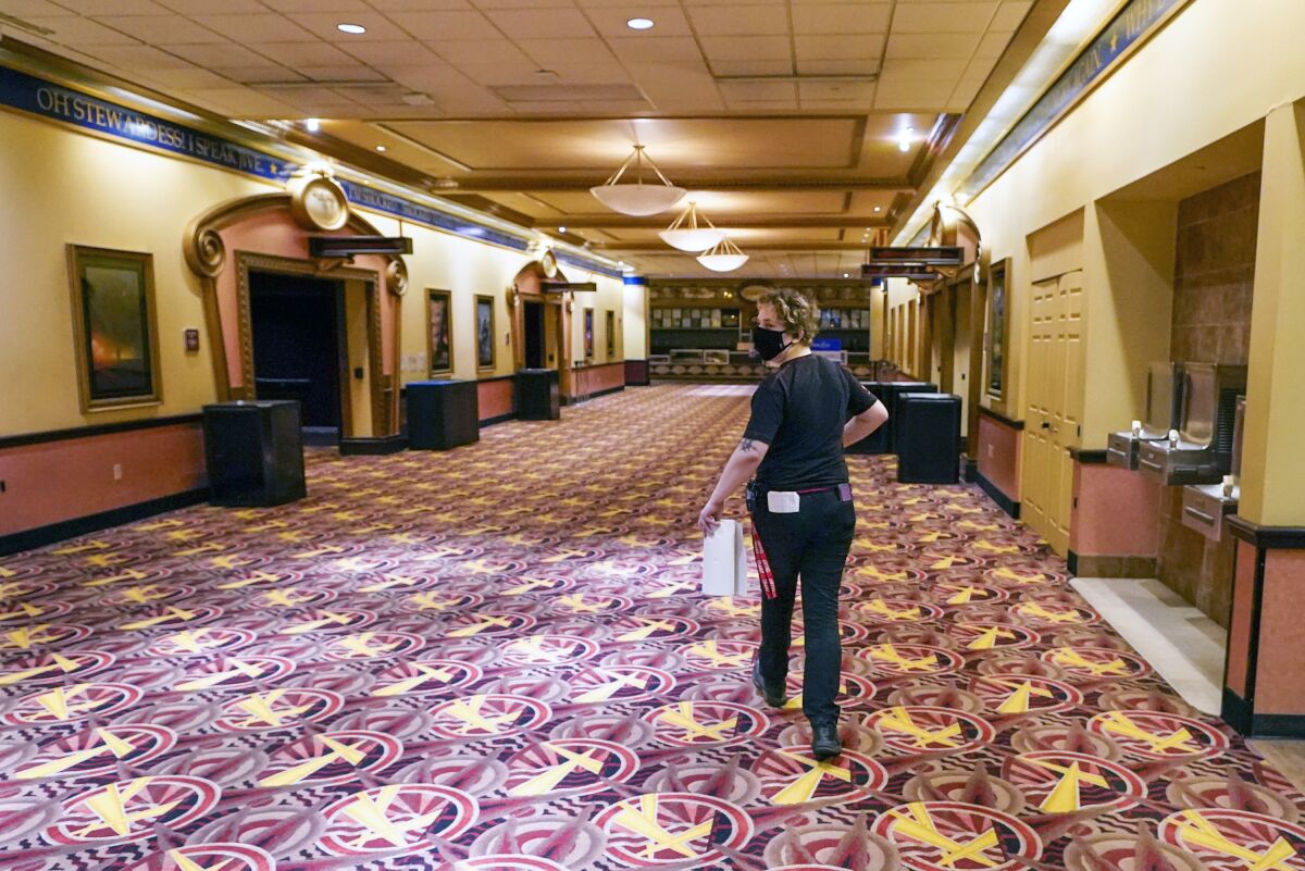 A masked worker in an empty hallway of a movie theater