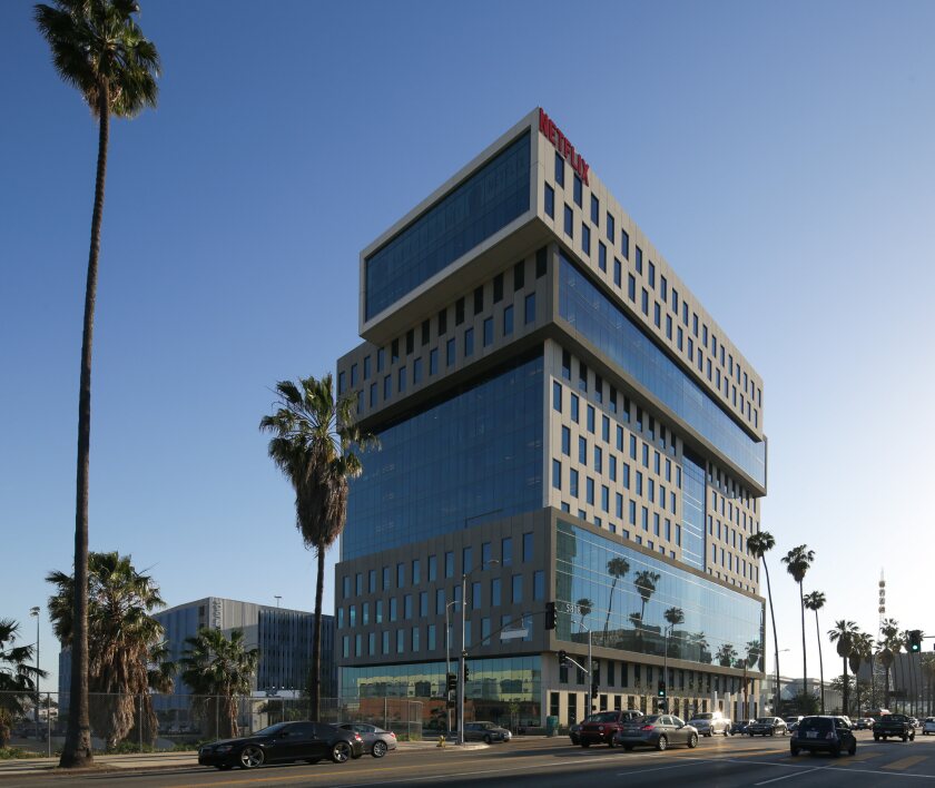A tall, gray building with many windows, surrounded by palm trees